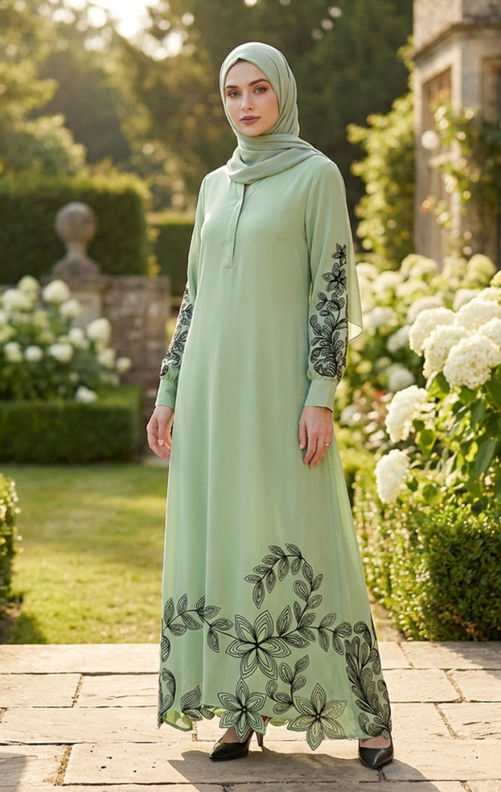 Woman in a light green dress with floral embroidery standing in a garden.