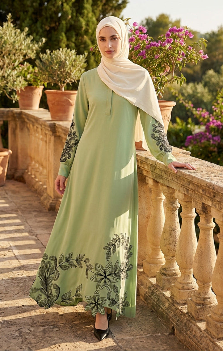 Woman in a green dress with floral patterns standing on a stone balcony with plants and flowers in the background.
