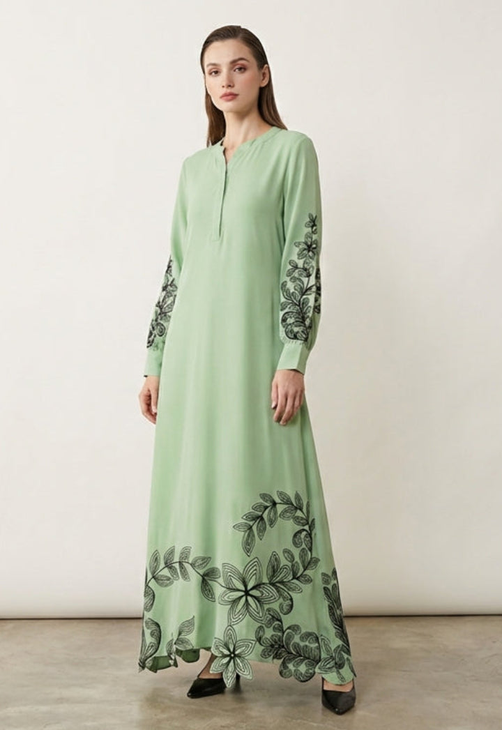 Woman wearing a long green dress with floral patterns in a minimalistic setting