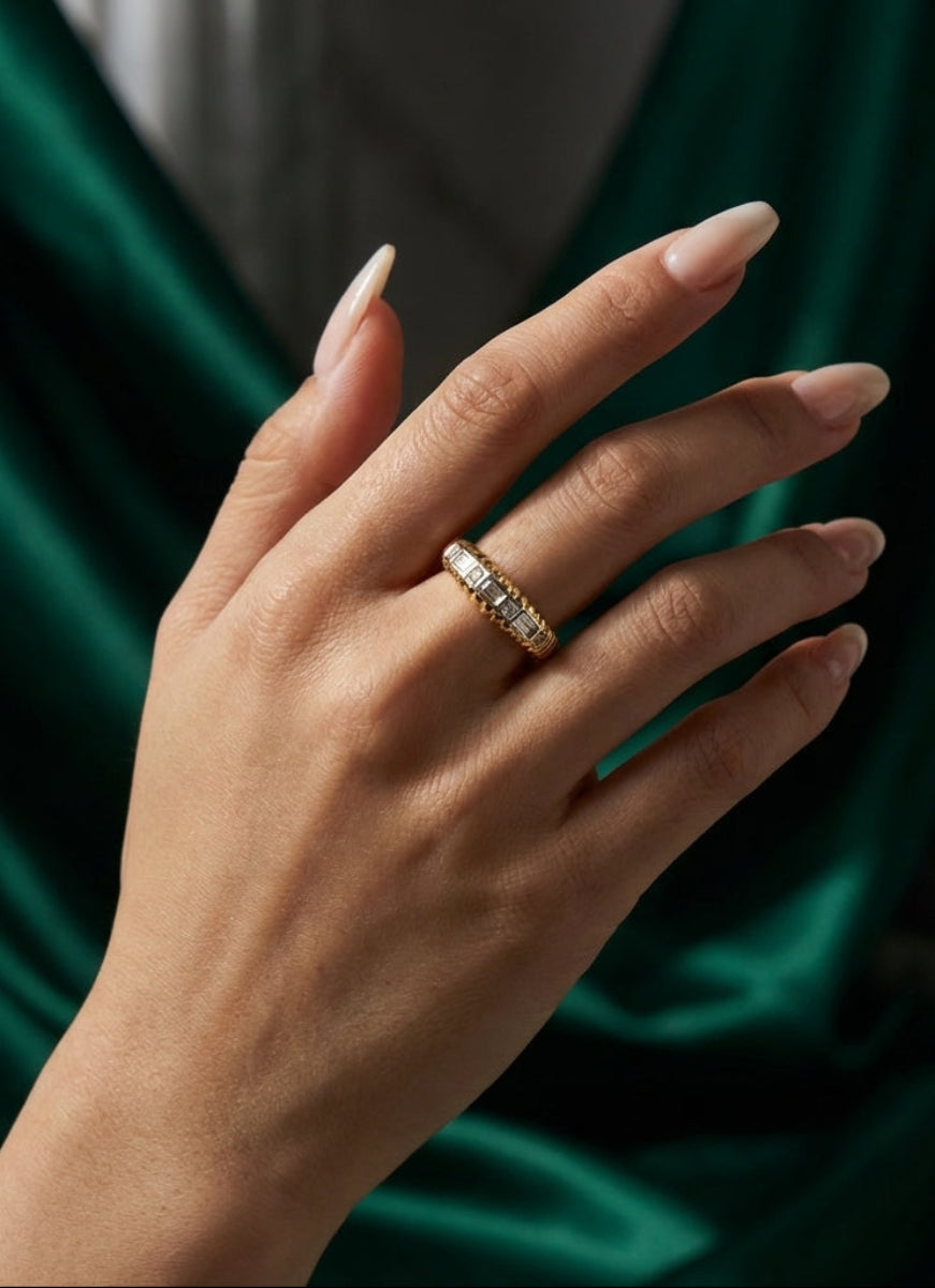 Hand wearing a gold ring with a green fabric background