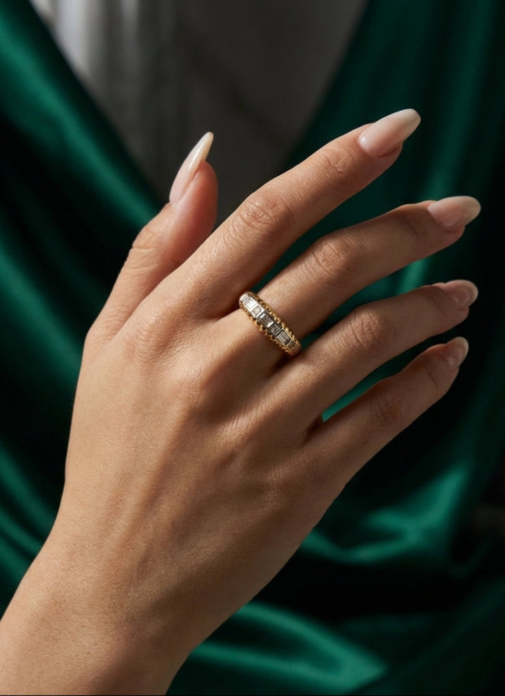 Hand wearing a gold ring with a green fabric background
