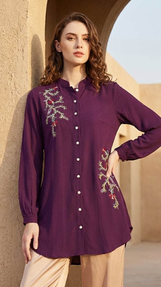 Woman wearing a purple embroidered shirt against a beige wall.