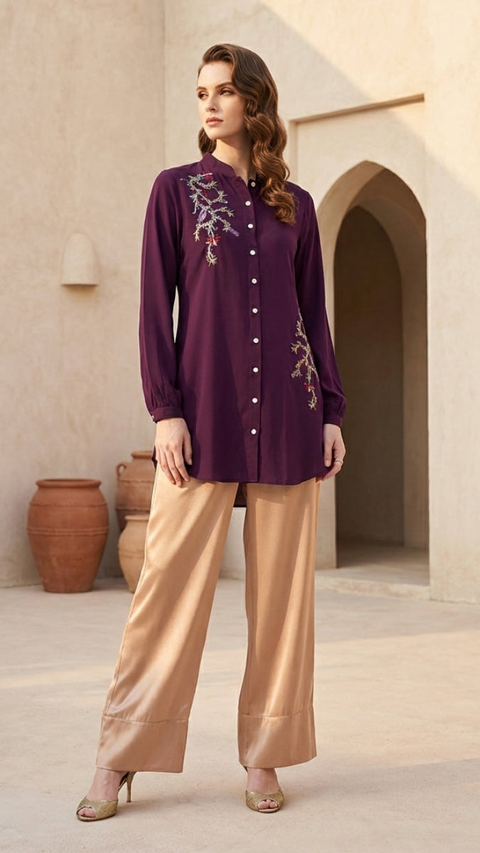 Woman wearing a purple embroidered top and beige pants in an architectural setting.