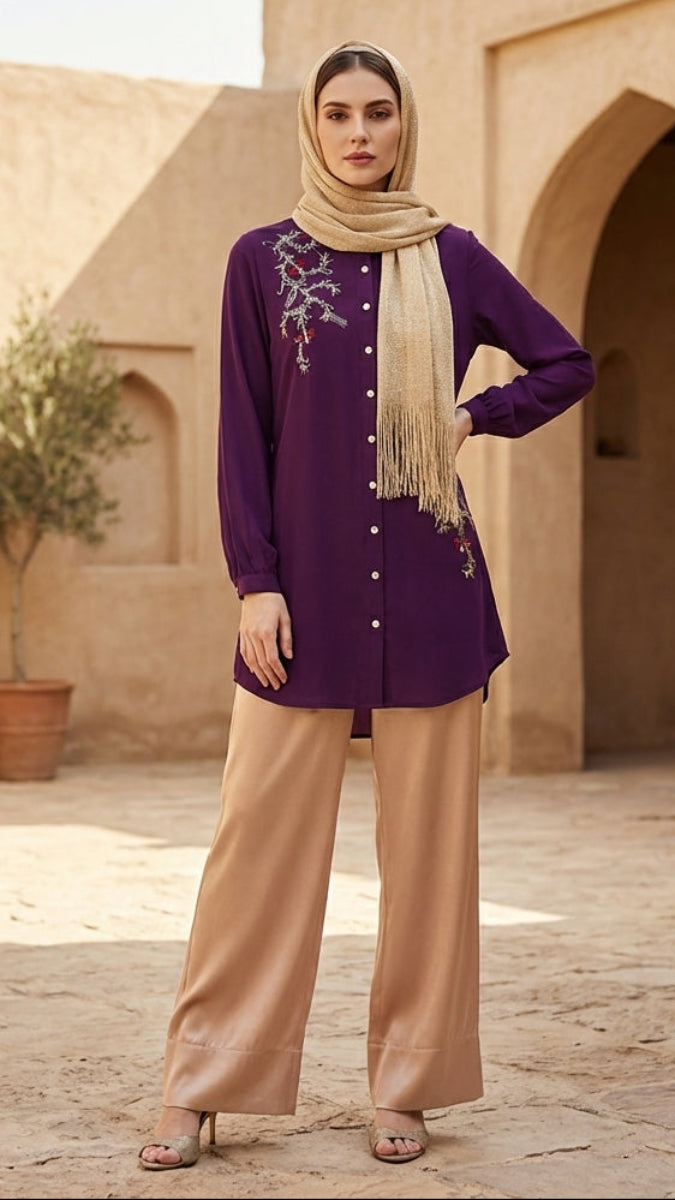 Woman in a purple top and beige pants standing in a sunlit courtyard with arches and potted plants.
