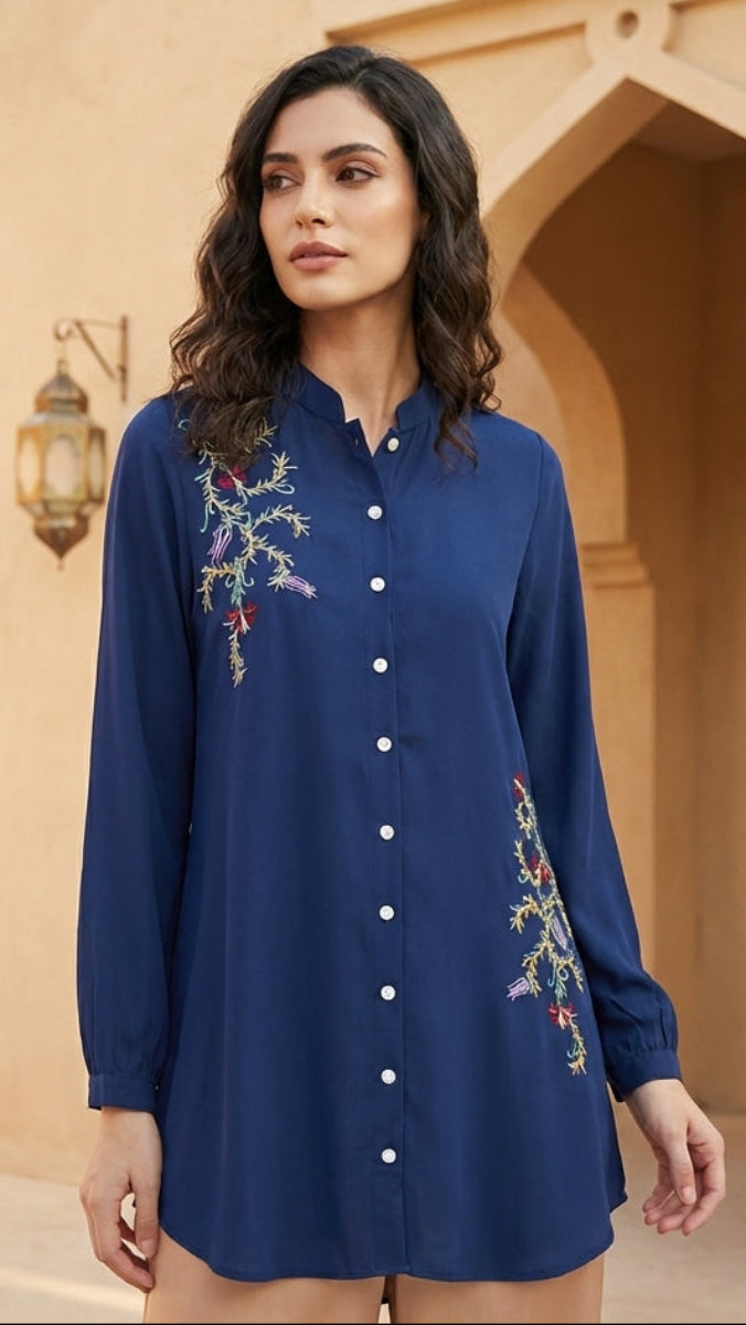 Woman wearing a blue embroidered dress in an outdoor setting with architectural elements.