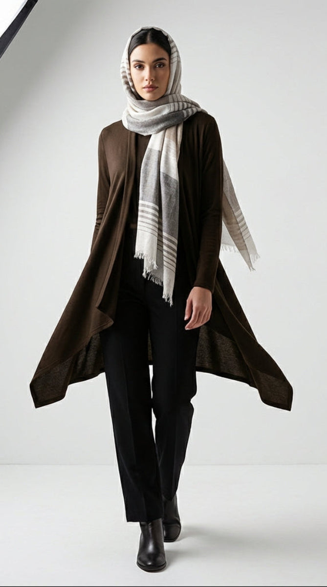 Woman wearing a long brown coat, black pants, and a light gray scarf on a white background