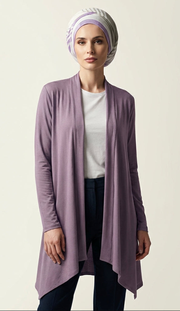 Woman wearing a light purple cardigan over a white shirt and dark pants, with a matching headscarf on a plain background.