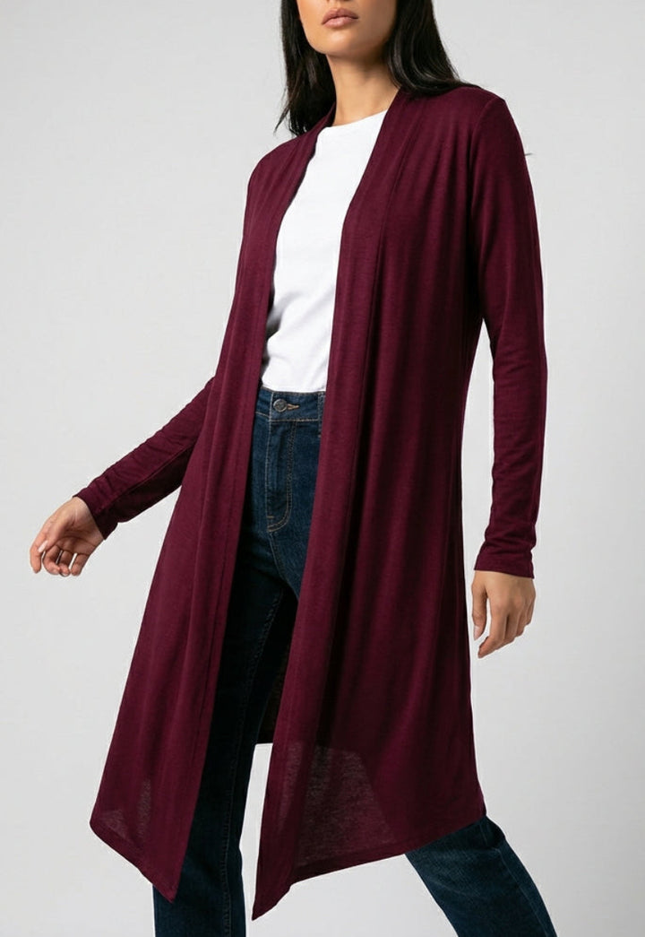 Woman wearing a burgundy cardigan over a white shirt and jeans on a gray background