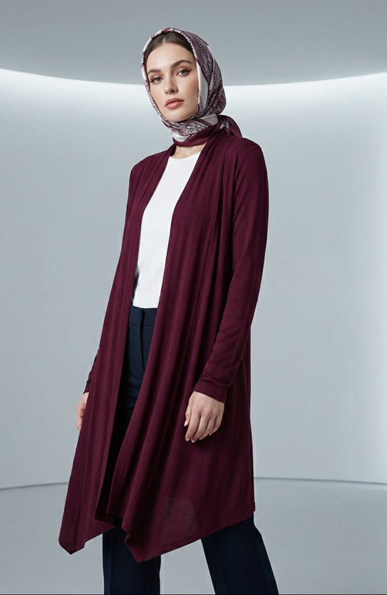 Woman wearing a burgundy cardigan over a white top and patterned headscarf in a minimalistic setting.