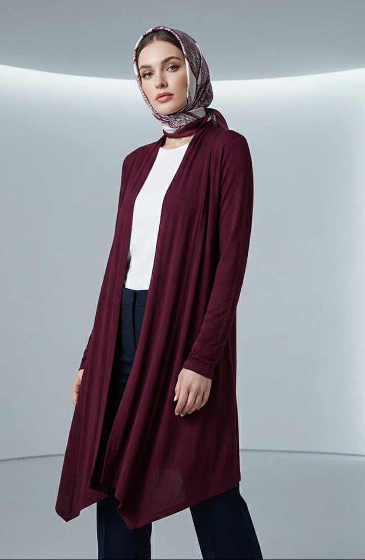Woman wearing a burgundy cardigan over a white top and patterned headscarf in a minimalistic setting.
