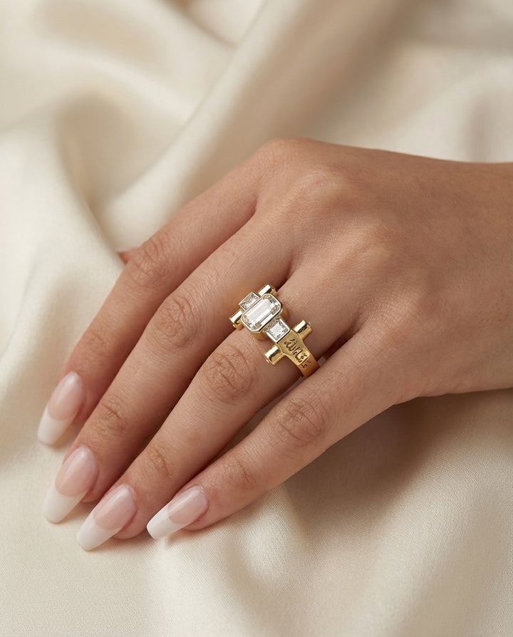 Gold ring with a large diamond on a hand against a beige fabric background