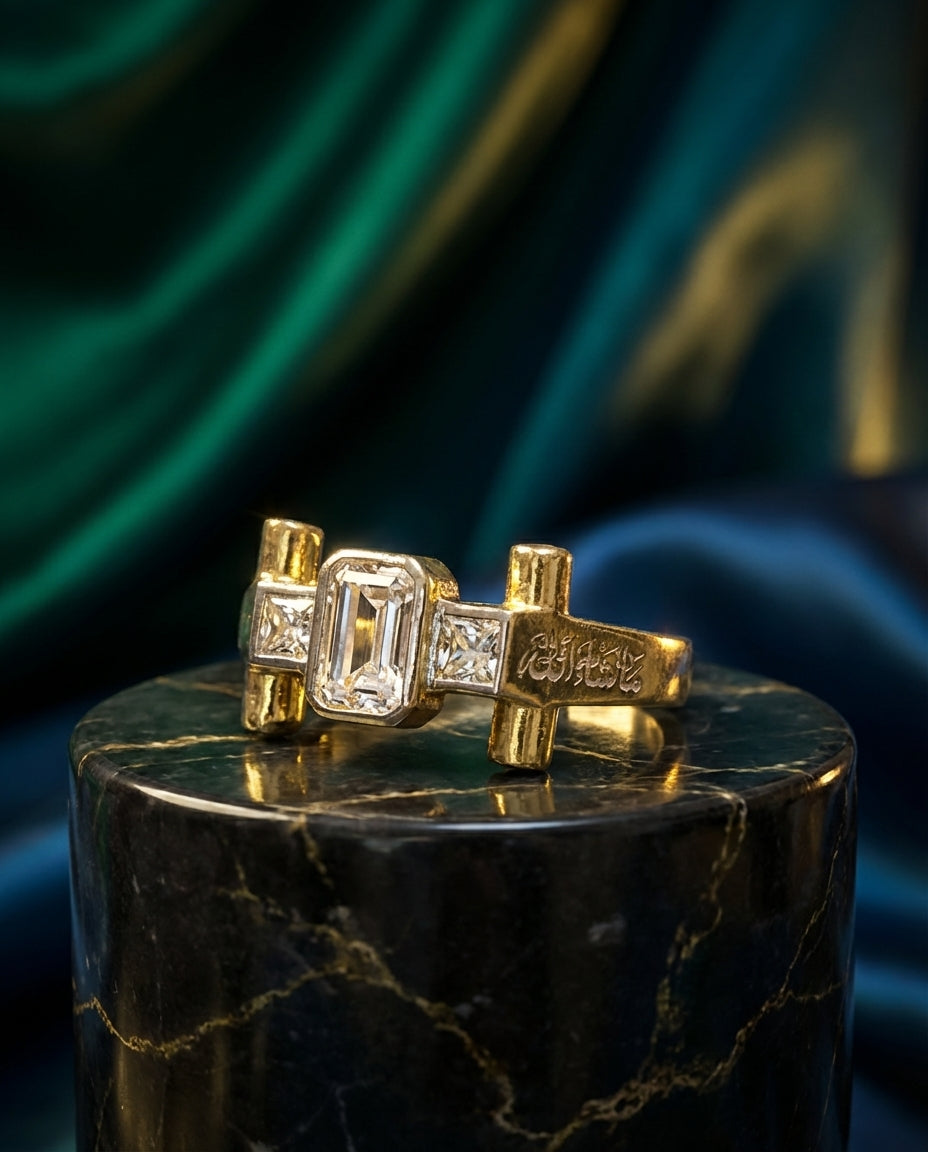 Gold ring with emerald-cut gemstone on a dark marble pedestal against a green and blue draped fabric background