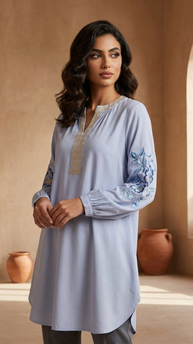 Woman wearing a light blue embroidered tunic in a warm-toned room.