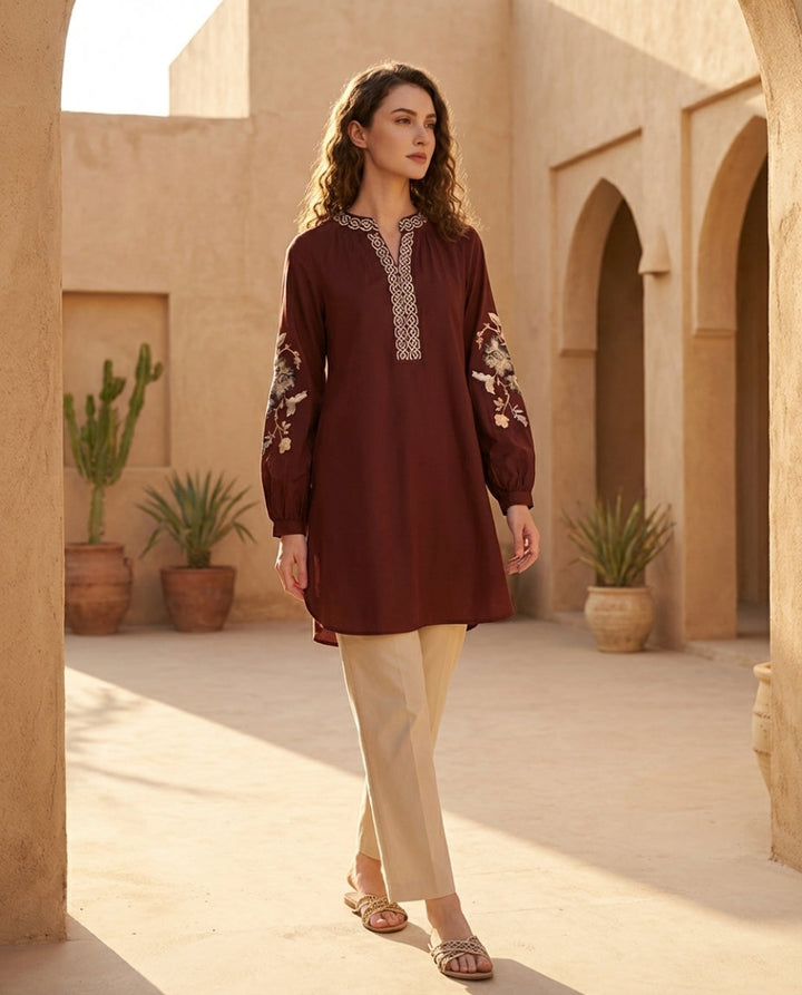Woman in a brown dress standing in a sunlit courtyard with arches and potted plants.