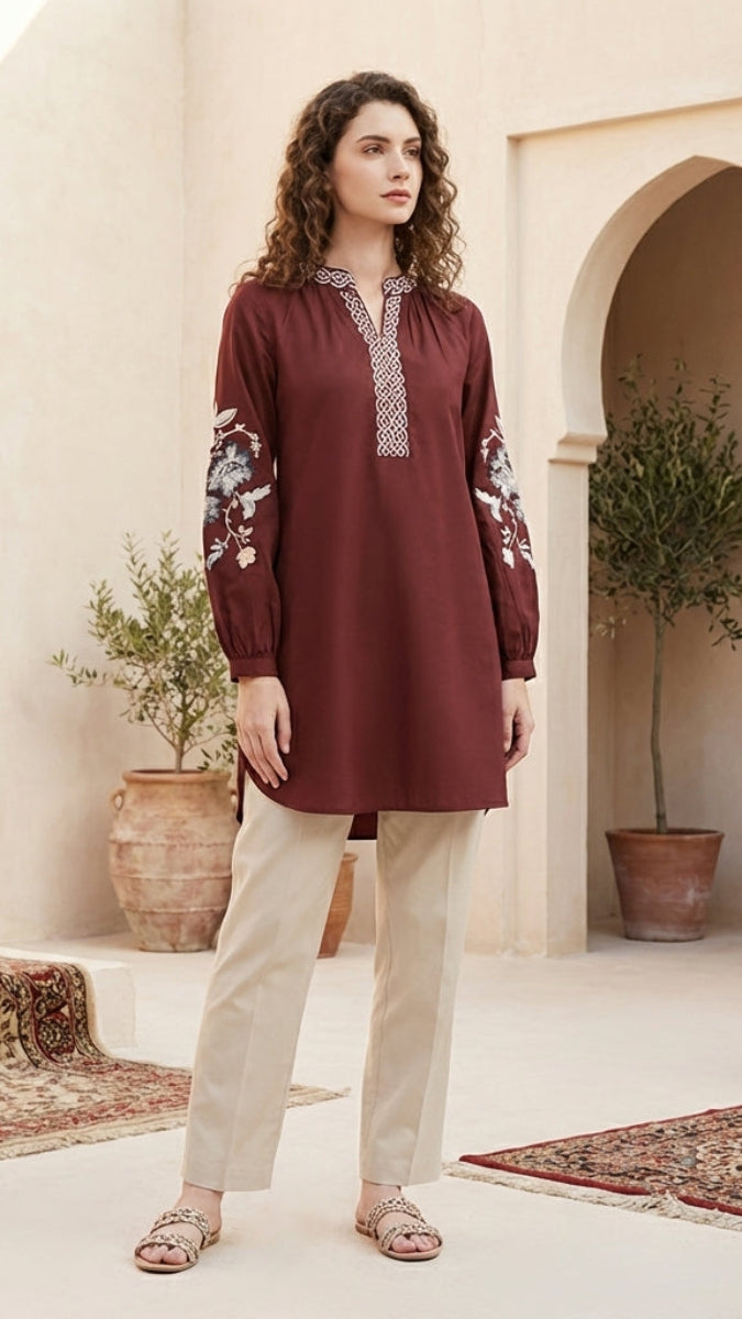 Woman in a burgundy top with floral patterns standing in a decorative outdoor setting with plants and rugs.