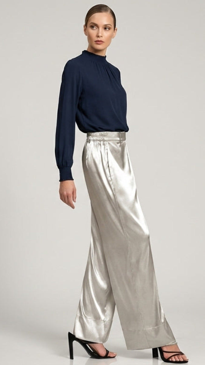 Woman wearing a navy sweater and silver pants on a gray background