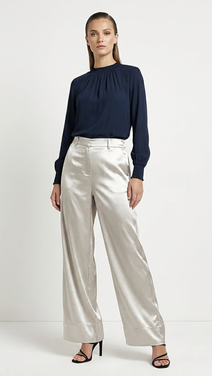 Woman wearing a navy top and silver pants on a white background