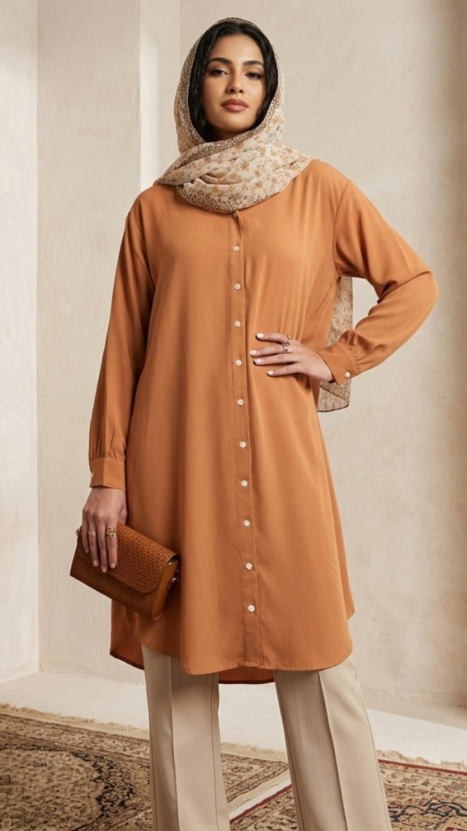Woman wearing a long orange dress with a matching hijab in a neutral setting