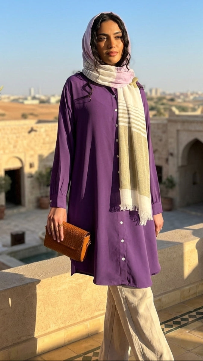 Woman in a purple outfit with a scarf standing on a sunlit rooftop with architectural elements and plants.