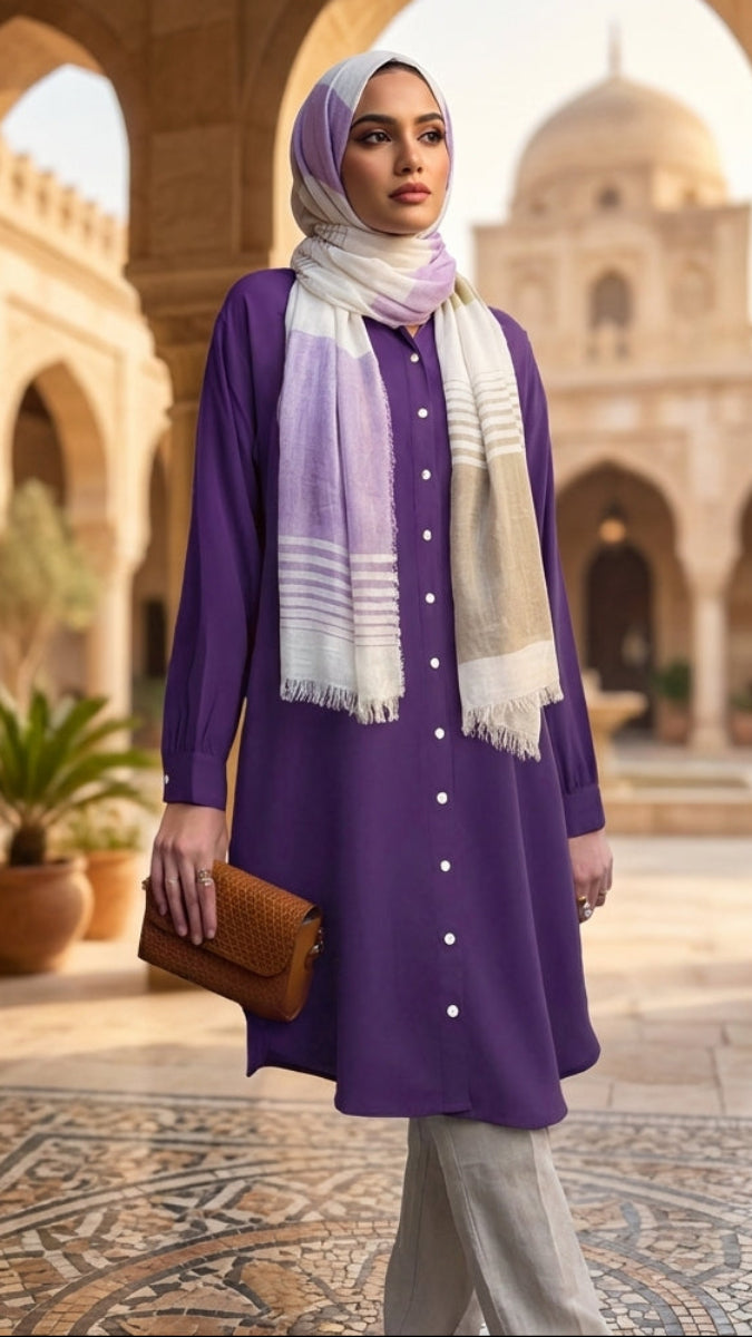 Woman in a purple outfit with a scarf standing in a historic courtyard.