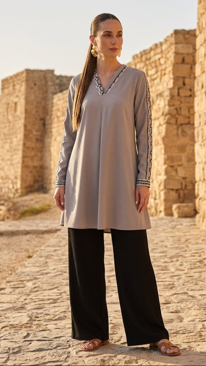 Woman in a long beige dress with black pants standing in front of stone ruins.