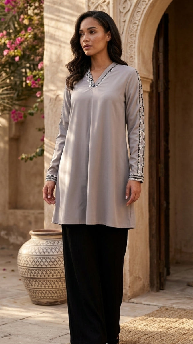 Woman in a light gray long-sleeve top with black pants standing in front of an architectural archway.
