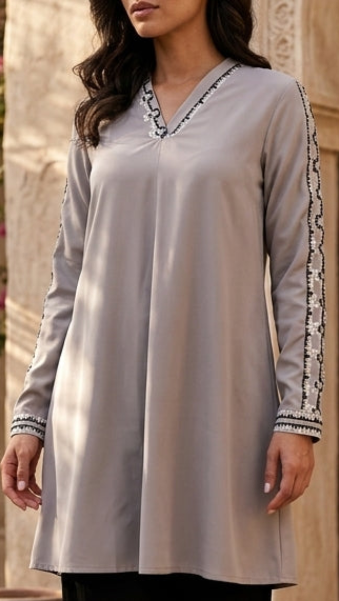 Woman in a light gray long-sleeve top with black pants standing in front of an architectural archway.