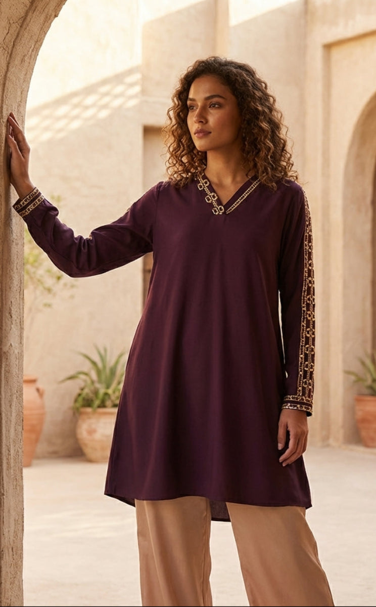 Woman in a purple dress with gold accents standing in a sunlit outdoor setting with arches and plants.