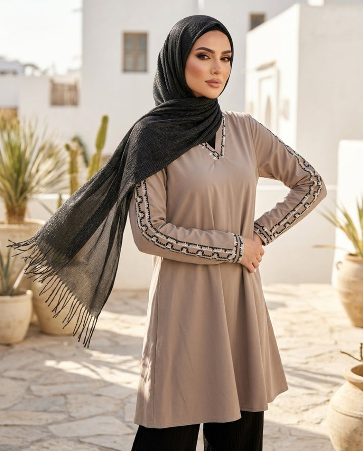 Woman wearing a beige dress with black hijab and embroidery outdoors.