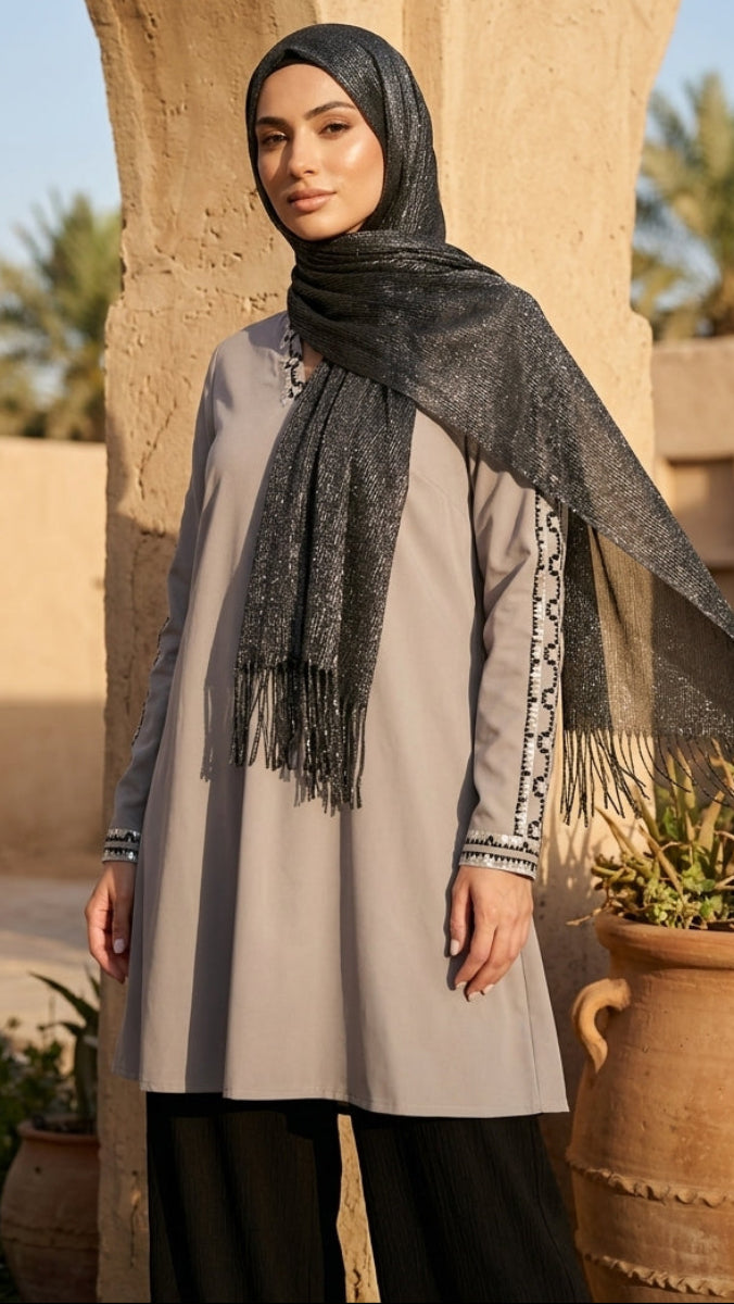 Woman wearing a hijab and long dress standing in front of an archway with palm trees in the background
