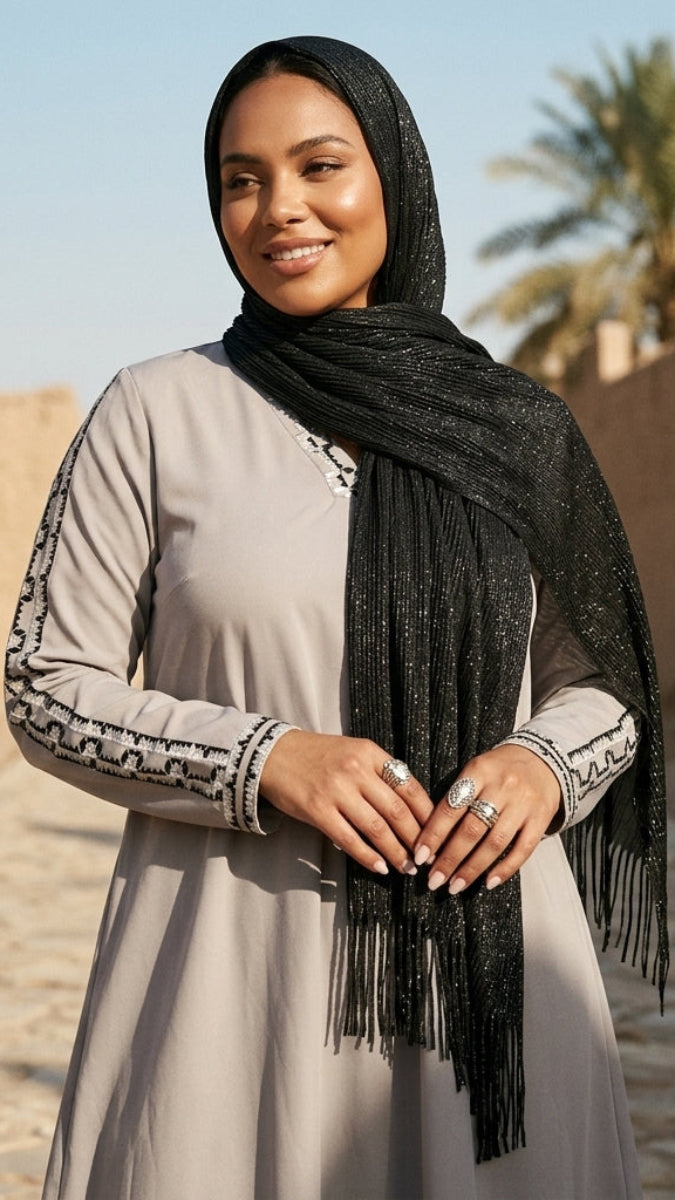 Woman wearing a hijab and long dress in a desert setting with palm trees.