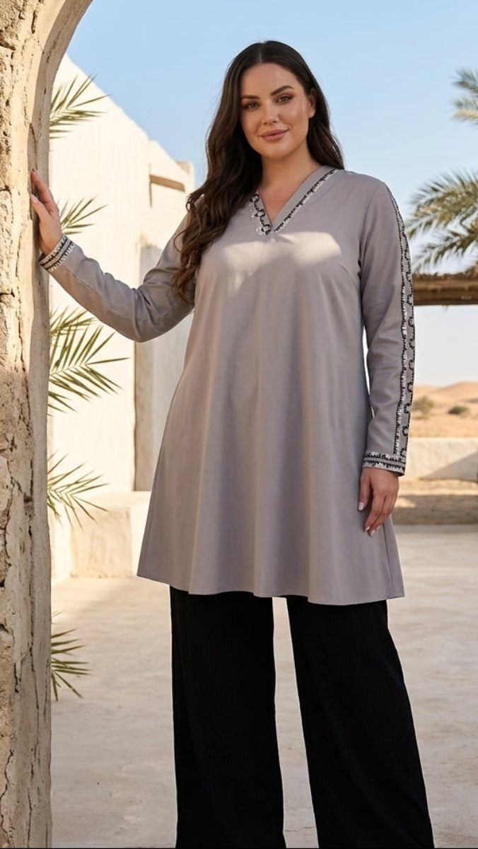 Woman in a long, light gray dress with black pants standing in a desert setting.