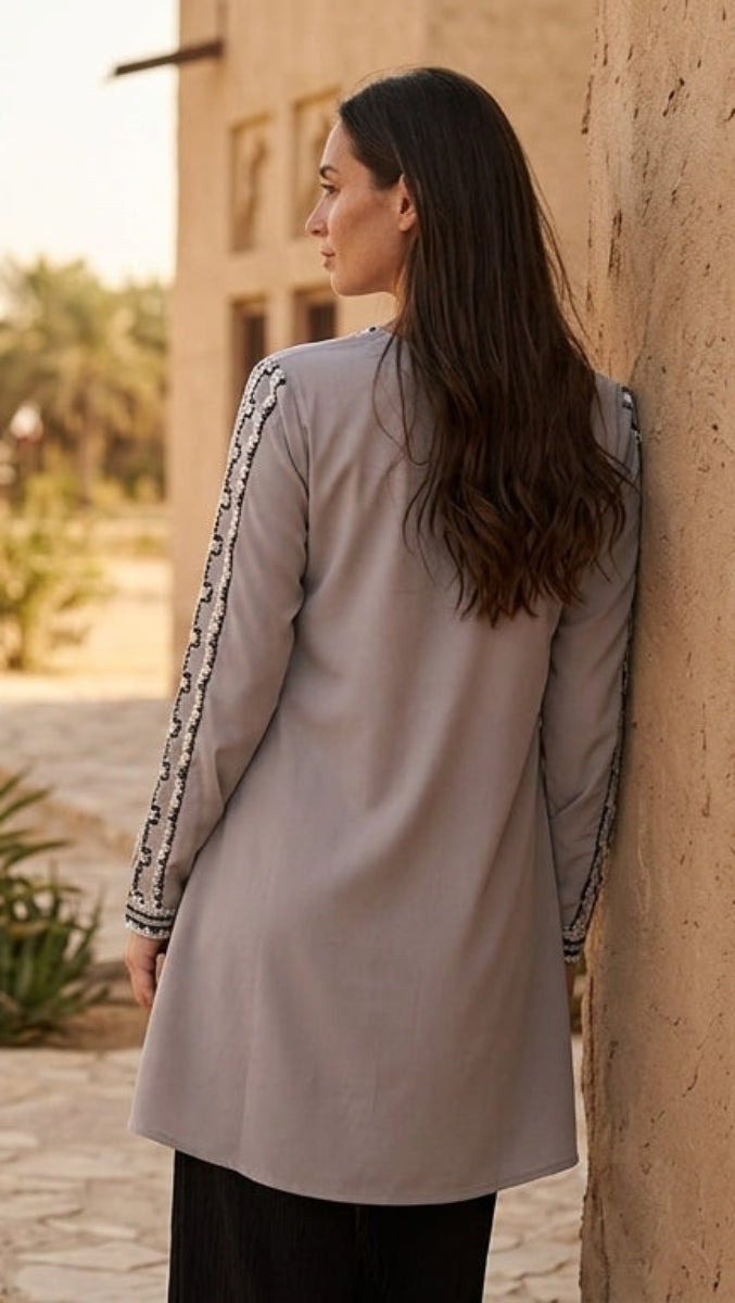 Woman in a long coat leaning against a stone wall with palm trees in the background