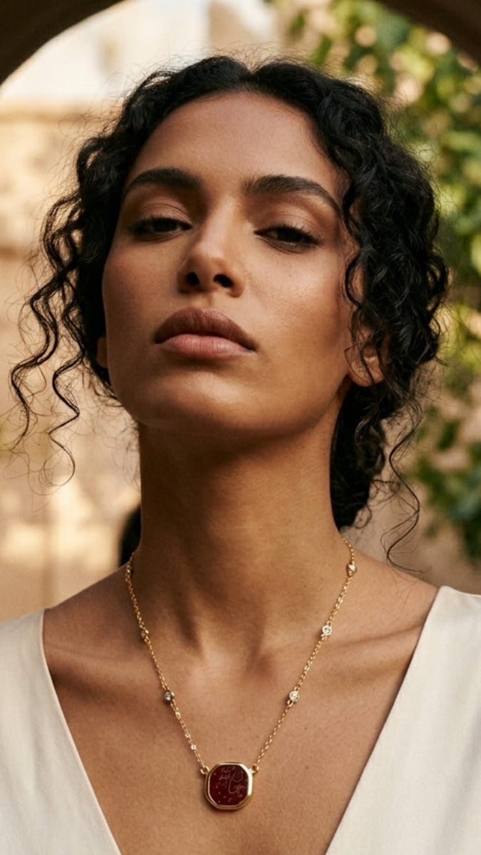 Woman wearing a gold necklace with a red pendant outdoors