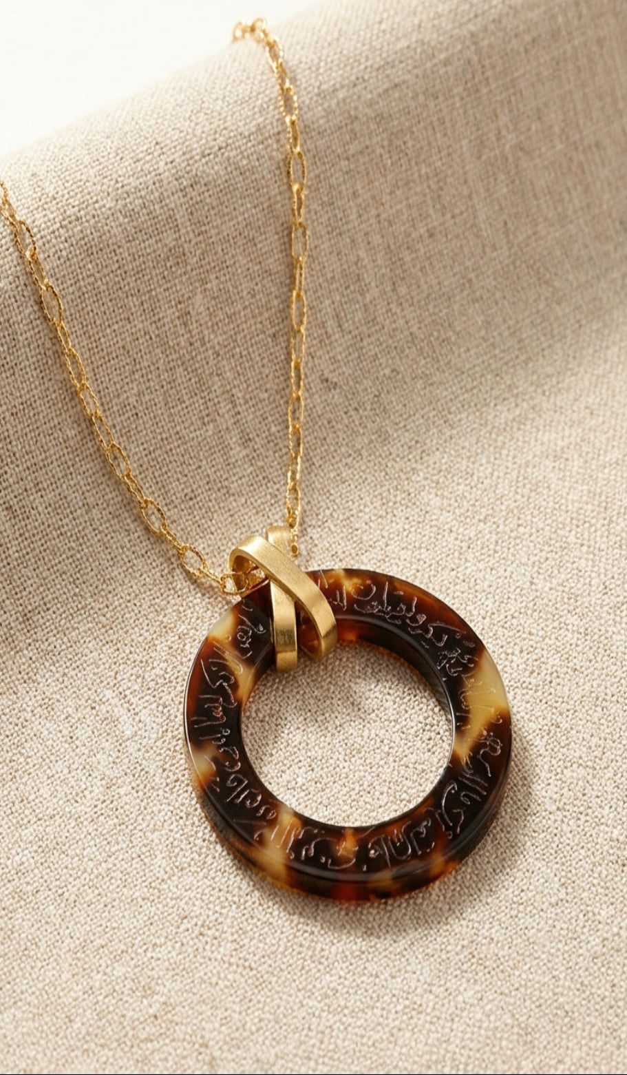 Tortoiseshell arabic calligraphy engraved pendant necklace on a beige fabric background
