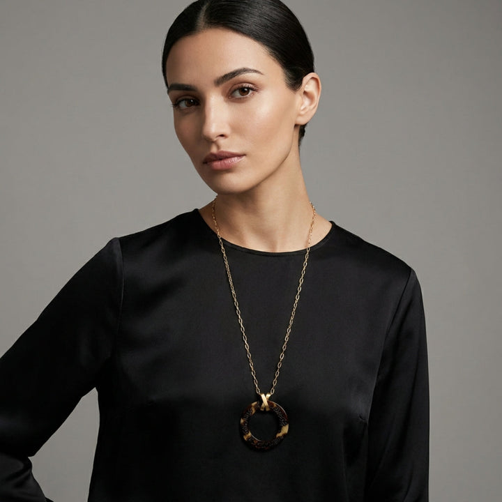 Woman wearing a black top and gold arabic calligraphy engraved totoise shell necklace against a gray background