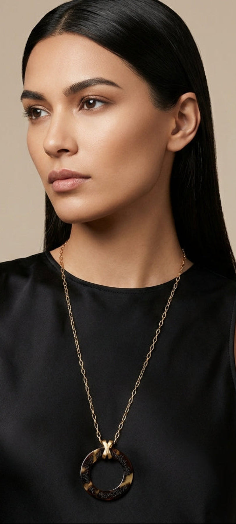 Woman wearing a black top with a gold arabic calligraphy engraved necklace against a beige background