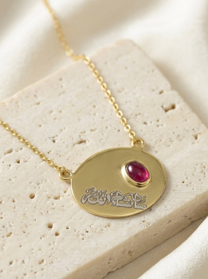 Gold necklace with a red gemstone on a textured beige surface