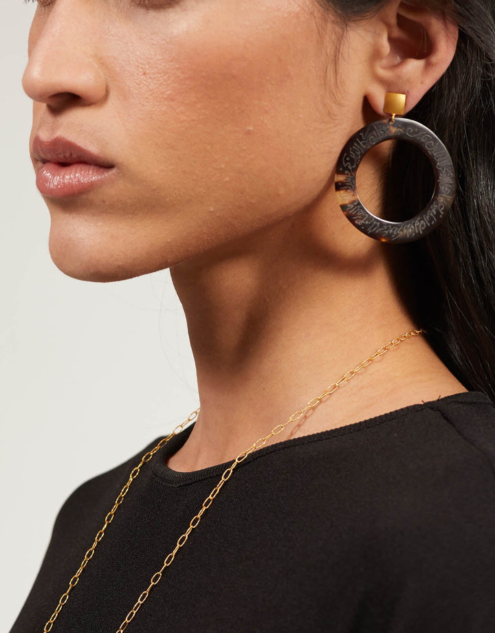 Woman wearing large hoop earrings with a plain background