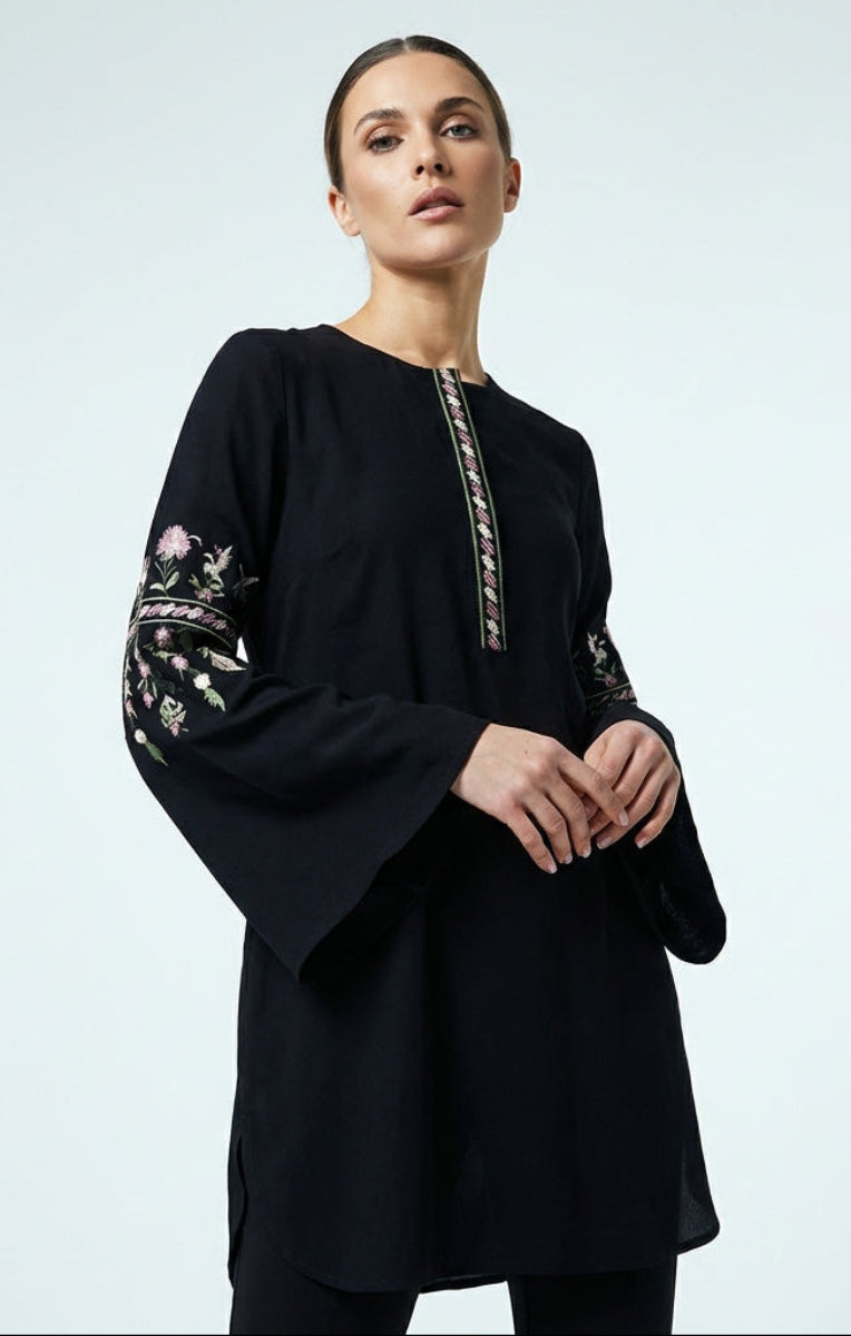 Woman wearing a black dress with floral embroidery on a light gray background