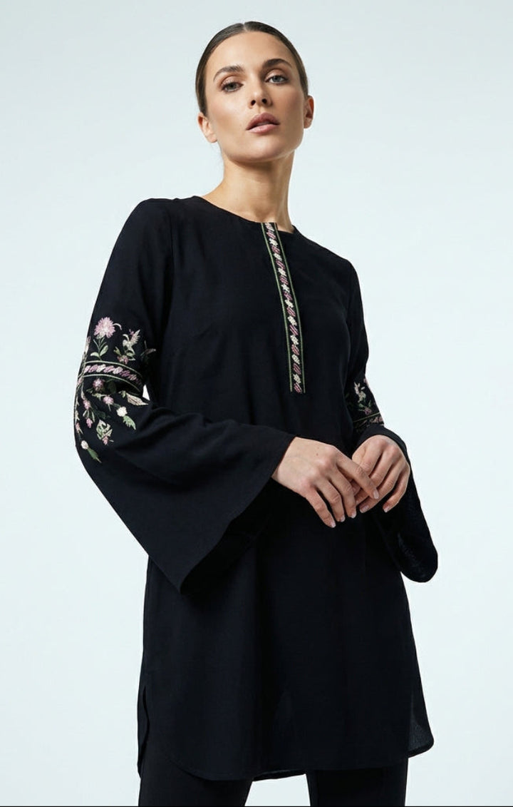 Woman wearing a black dress with floral embroidery on a light gray background