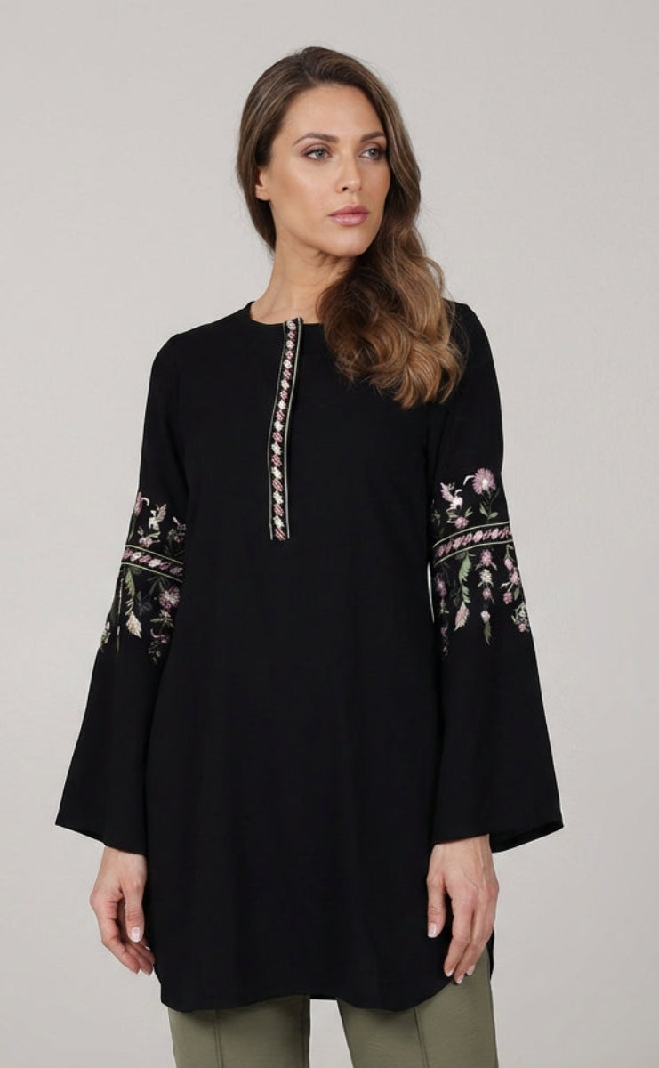 Woman wearing a black tunic with floral embroidery on a gray background