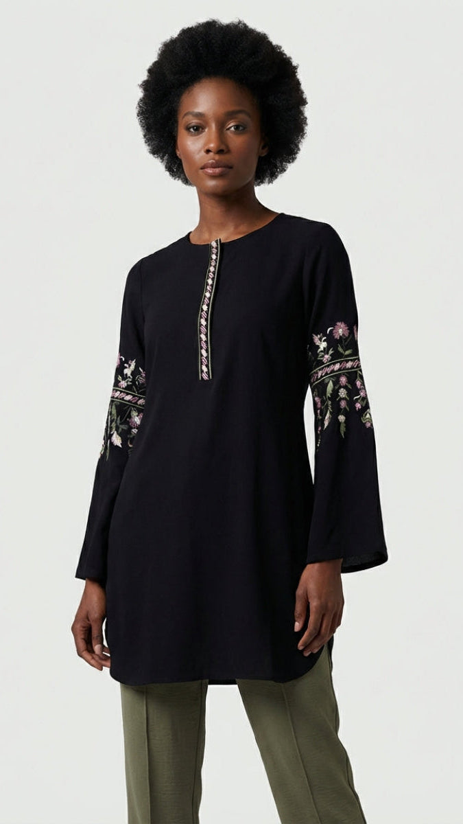 Woman wearing a black long-sleeve top with floral embroidery on a white background