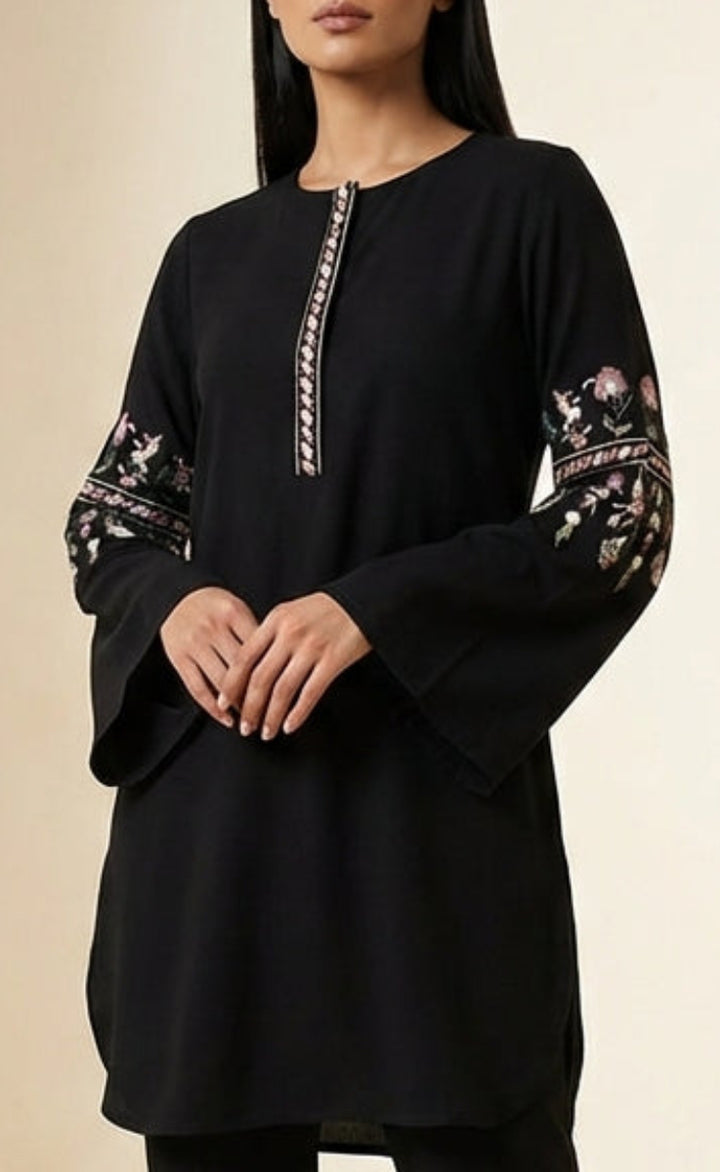 Woman wearing a black outfit with floral embroidery on sleeves against a beige background