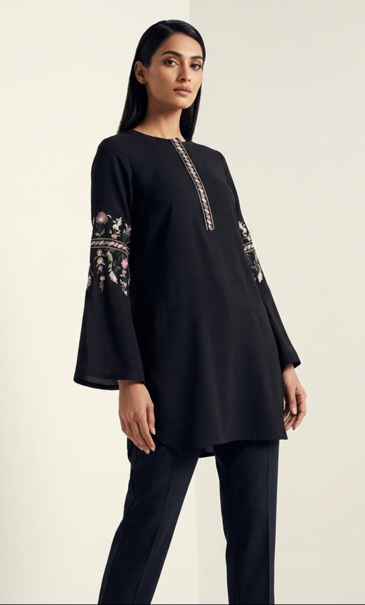 Woman wearing a black long-sleeve top with embroidery on a plain background