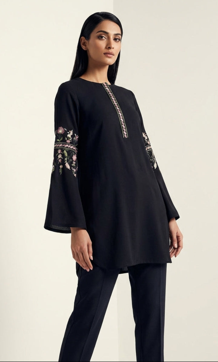 Woman wearing a black long-sleeve top with embroidery on a plain background