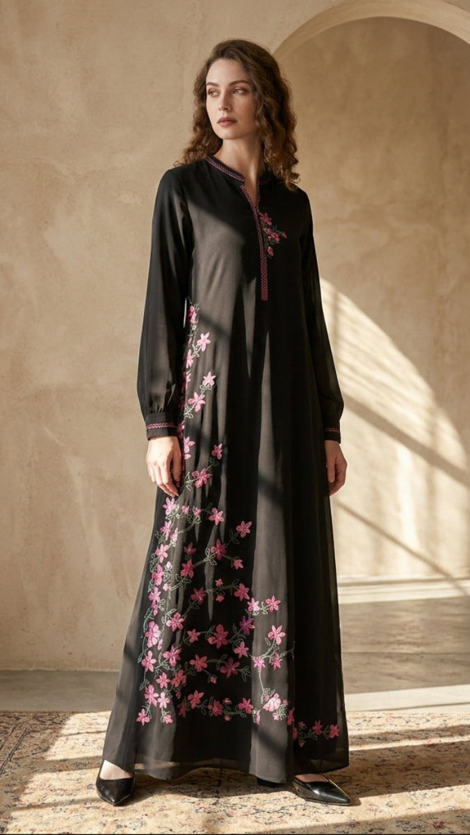 Woman wearing a black dress with pink floral embroidery in a sunlit room.