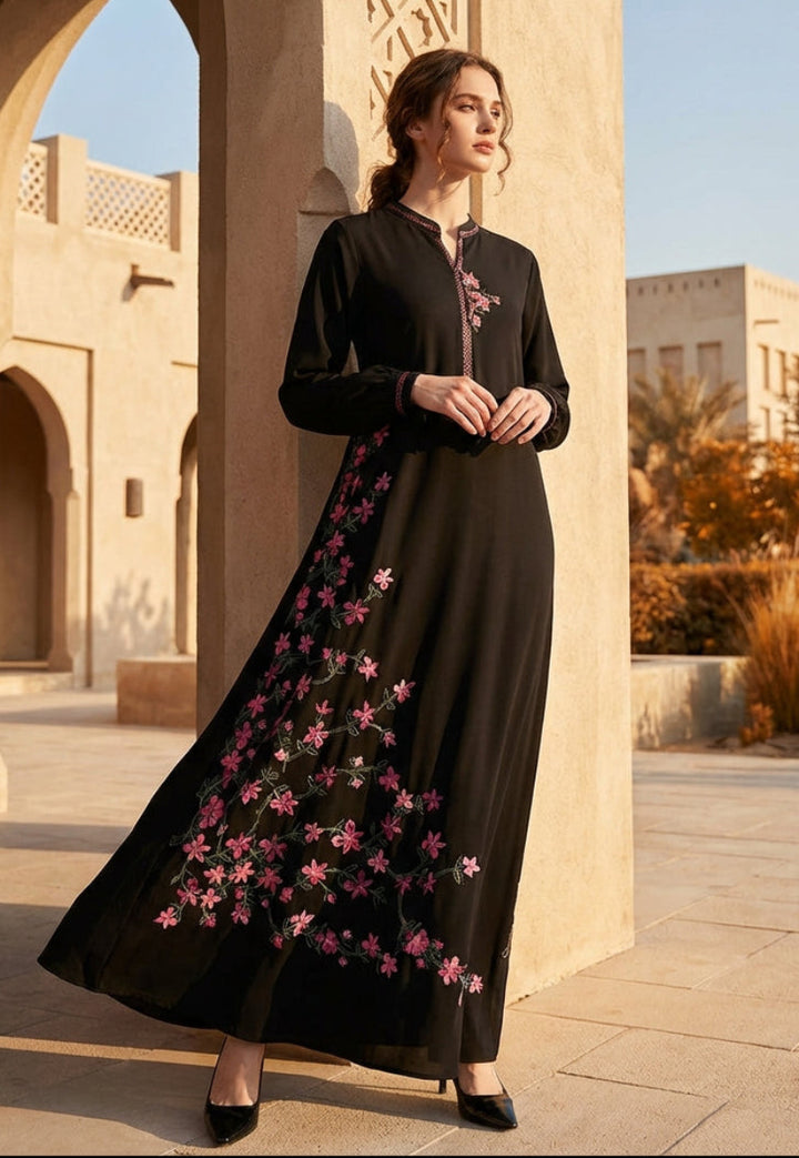 Woman in a black dress with pink floral embroidery standing in front of an architectural archway.