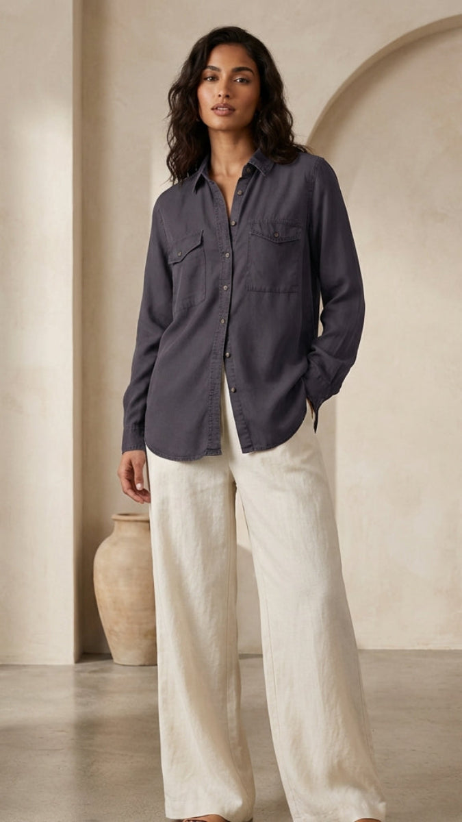 Woman wearing a dark shirt and light pants standing against a beige wall.