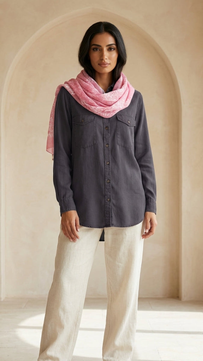 Woman wearing a dark shirt and light pants with a pink scarf in a sunlit room.